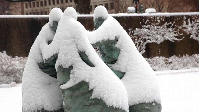 Three stone sulptures of people holding hands in a circle covered in snow Last Conversation Piece sculpture by Juan Munoz