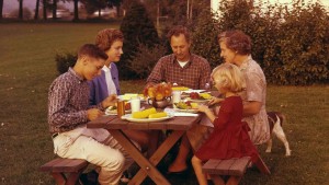 A family eating at picnic table in their backyard circa 1950s