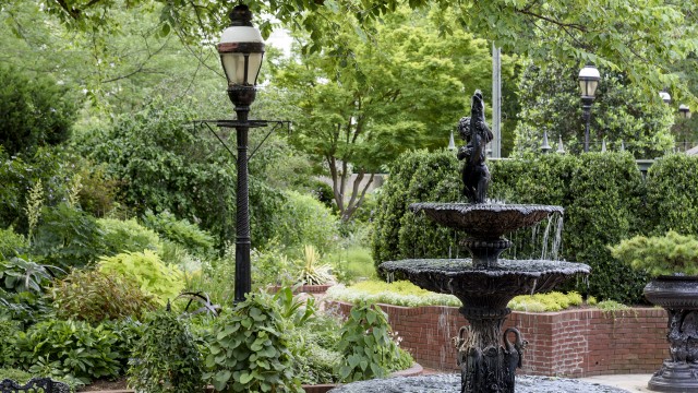 Cast iron three-tiered fountain with bird motif framed by raised brick beds planted with varying shades of green