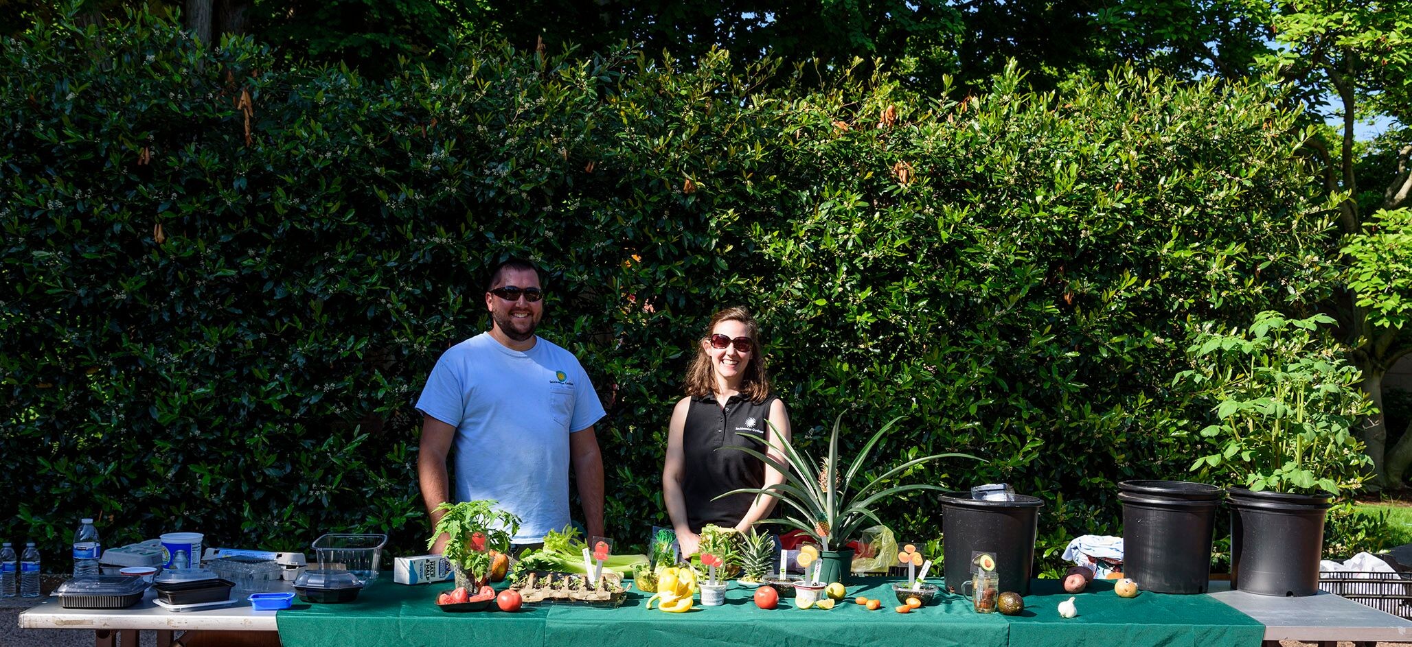 Two Smithsonian Gardens staff members stand behind table of plants grown from food scraps