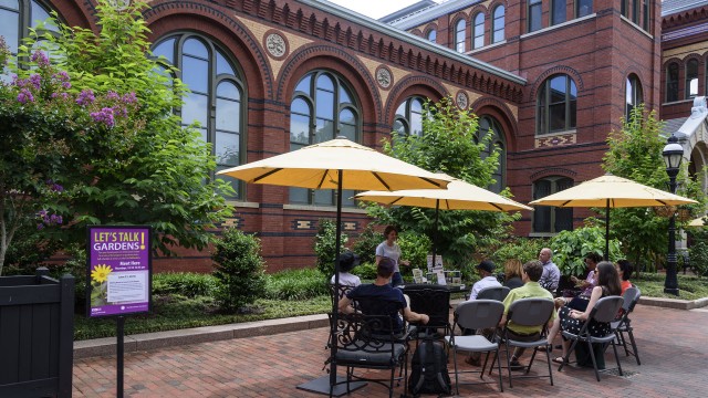 Horticulturist leading a "Let's Talk Gardens" program in the Enid A. Haupt garden. People are sitting in chairs under umbrellas.