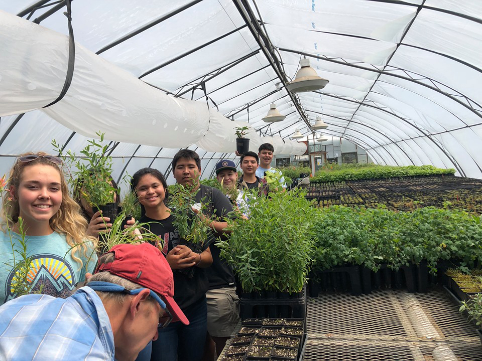 Teens in greenhouse holding potted seedlings