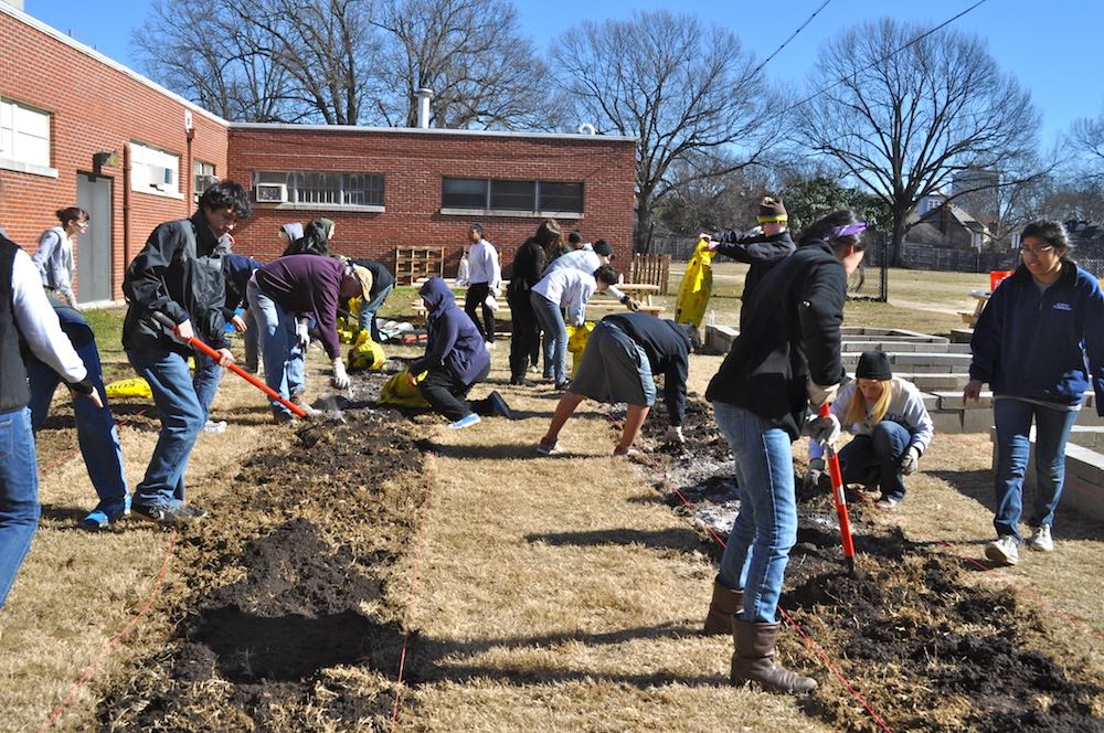 People in coats digging in ground with yellowed grass