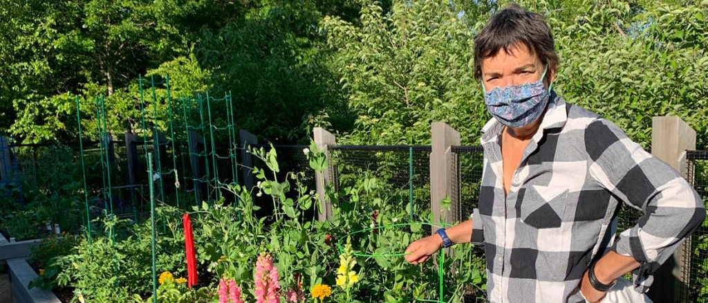 Person in plaid wearing a mask with their hand on a garden fence