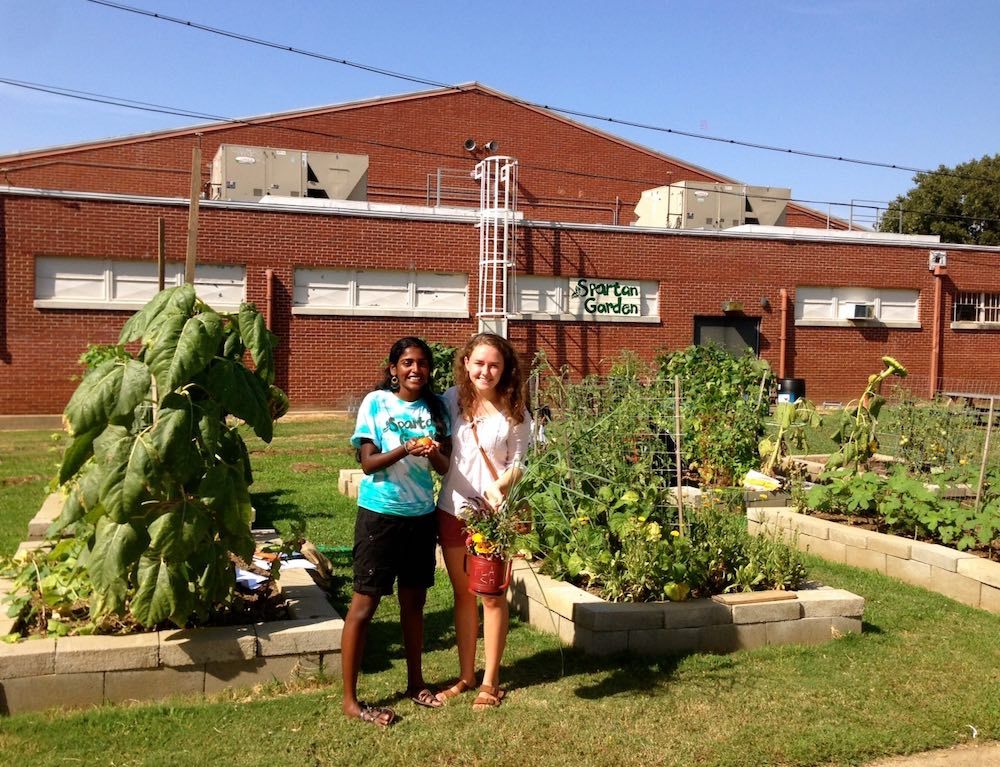 Two teenagers holding vegetables beside garden beds