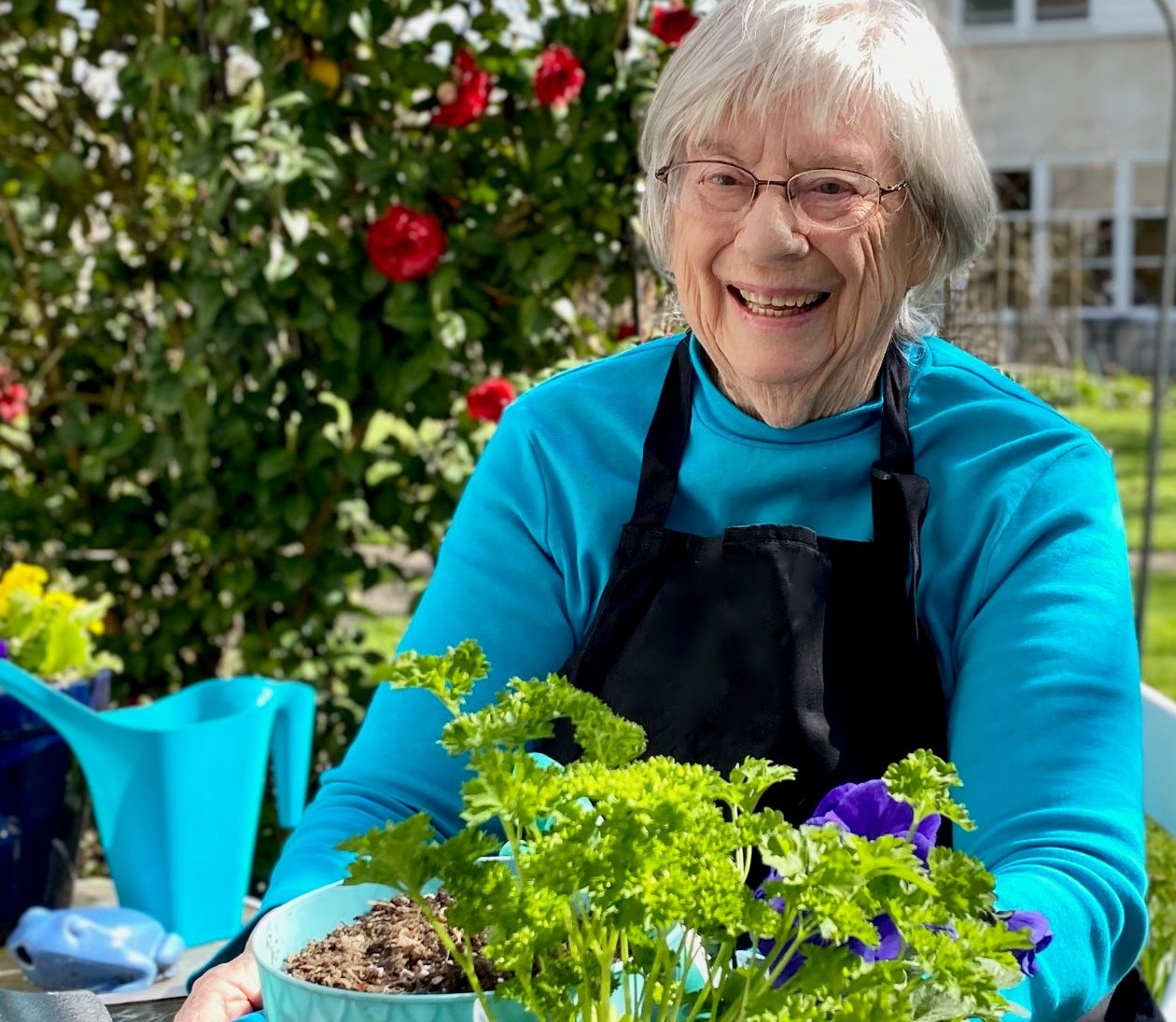 Woman with grey hair wearing glasses and apron holds pot of soil