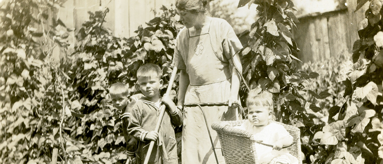 Three children and mother near vine covered fence